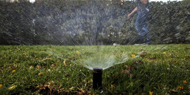FILE - In this June 5, 2015, file photo, Tony Corcoran records sprinklers watering the lawn in front of a house in Beverly Hills, Calif. In the coming months, state officials will undertake a monumental task of rewriting conservation orders for a fifth year of drought. (AP Photo/Jae C. Hong, File)